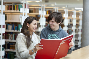 Studierende mit Atlas in der Universitätsbibliothek